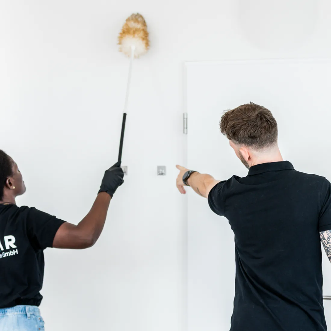 Zwei Personen aus dem Polar-Team entstauben bei der Büroreinigung Wand und Leuchte in einem Büro